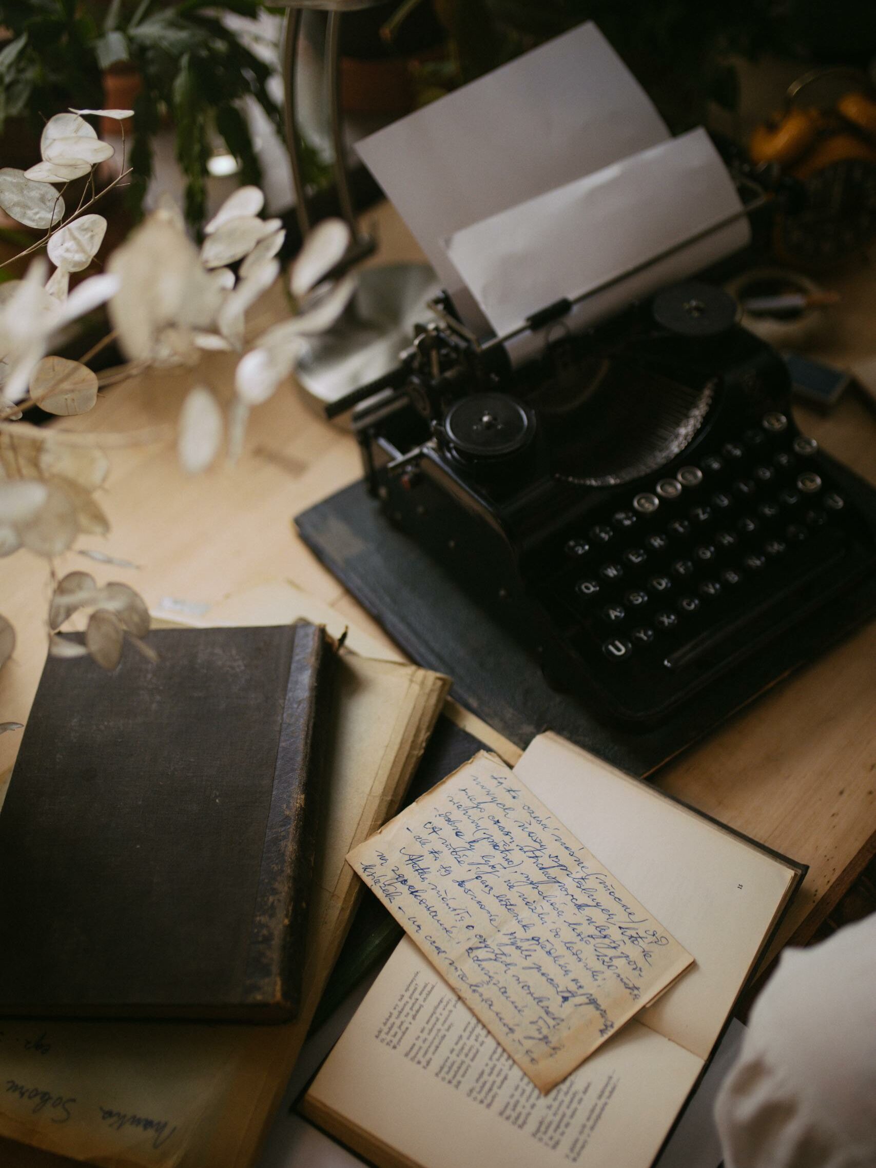 A Black Typewriter with a Bond Paper Beside a Book on a Wooden Table